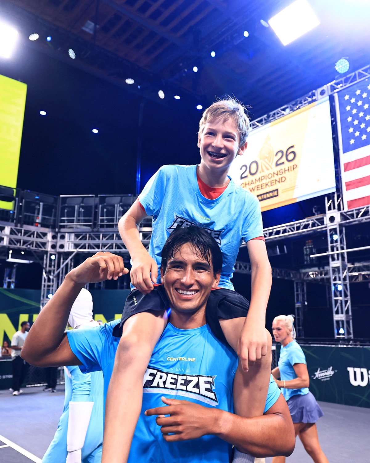 A young ball keeper riding on the shoulders of a Freeze player, both grinning, under Championship Weekend signage.